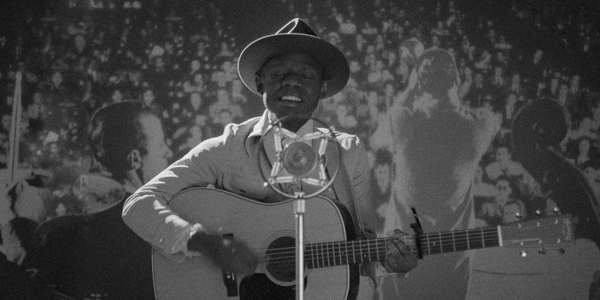monochrome of j.s. ondura in a hat and suit playing guitar while singing